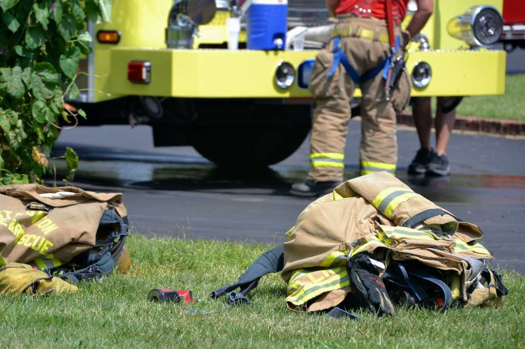 Fire gear lying on the ground with firemen and a firetruck in the background